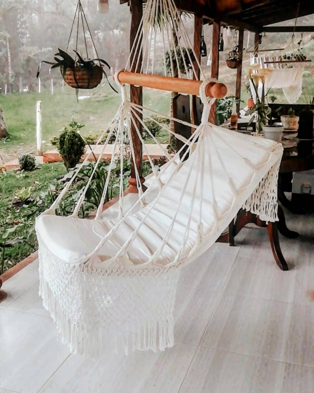 Silla hamaca colgante de macramé crudo con flecos, en una terraza con jardín